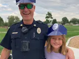 Police officer and a young girl posing with their police hats on at a park.